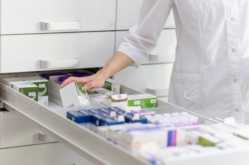 Pharmacist holding medicine box and capsule pack in pharmacy drugstore.
